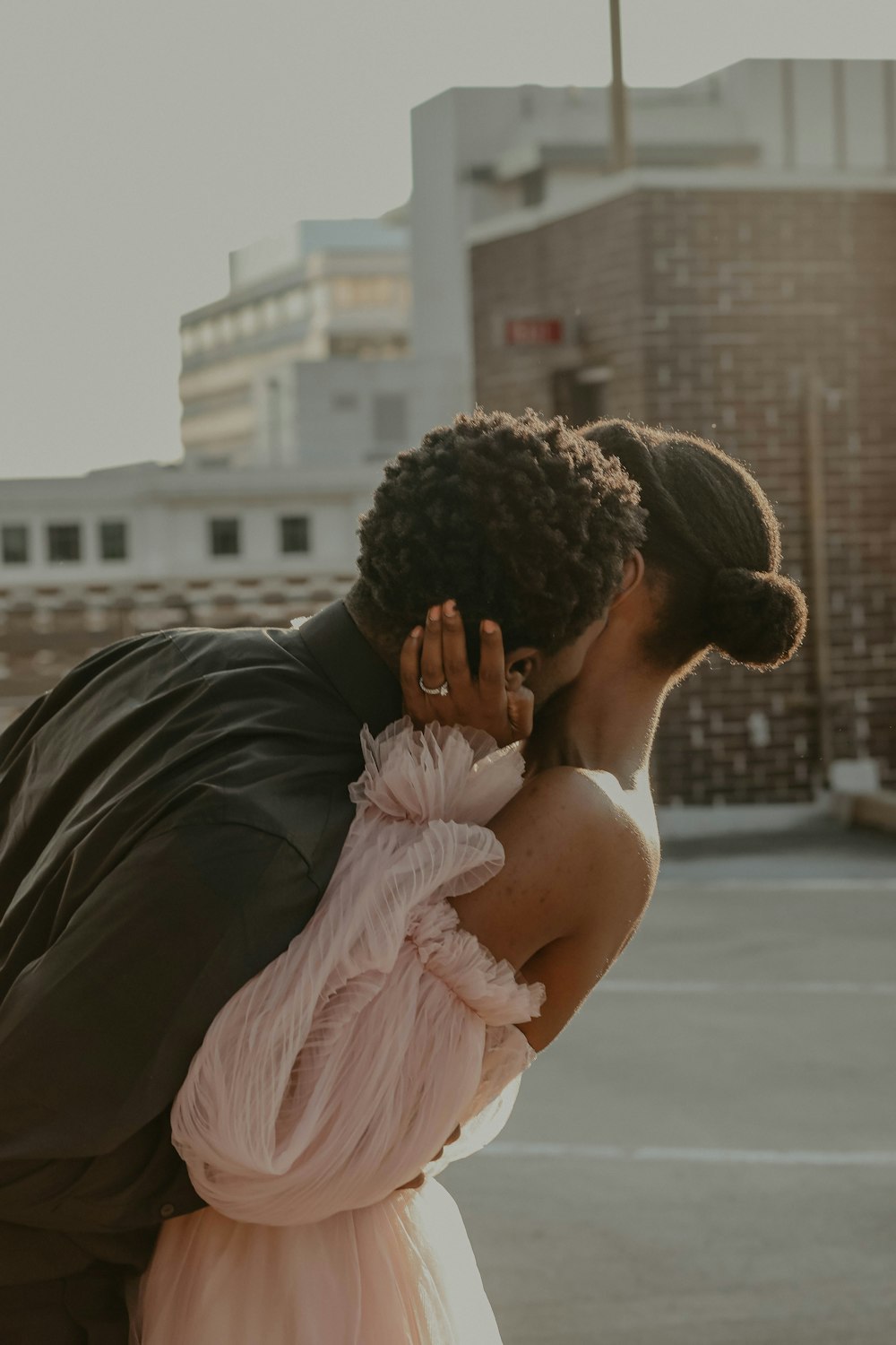 homme en costume noir embrassant femme en robe rose pendant la journée