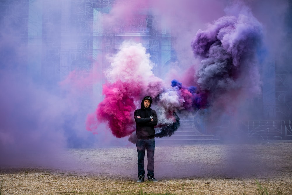 person in black jacket and black pants standing on brown field with pink smoke