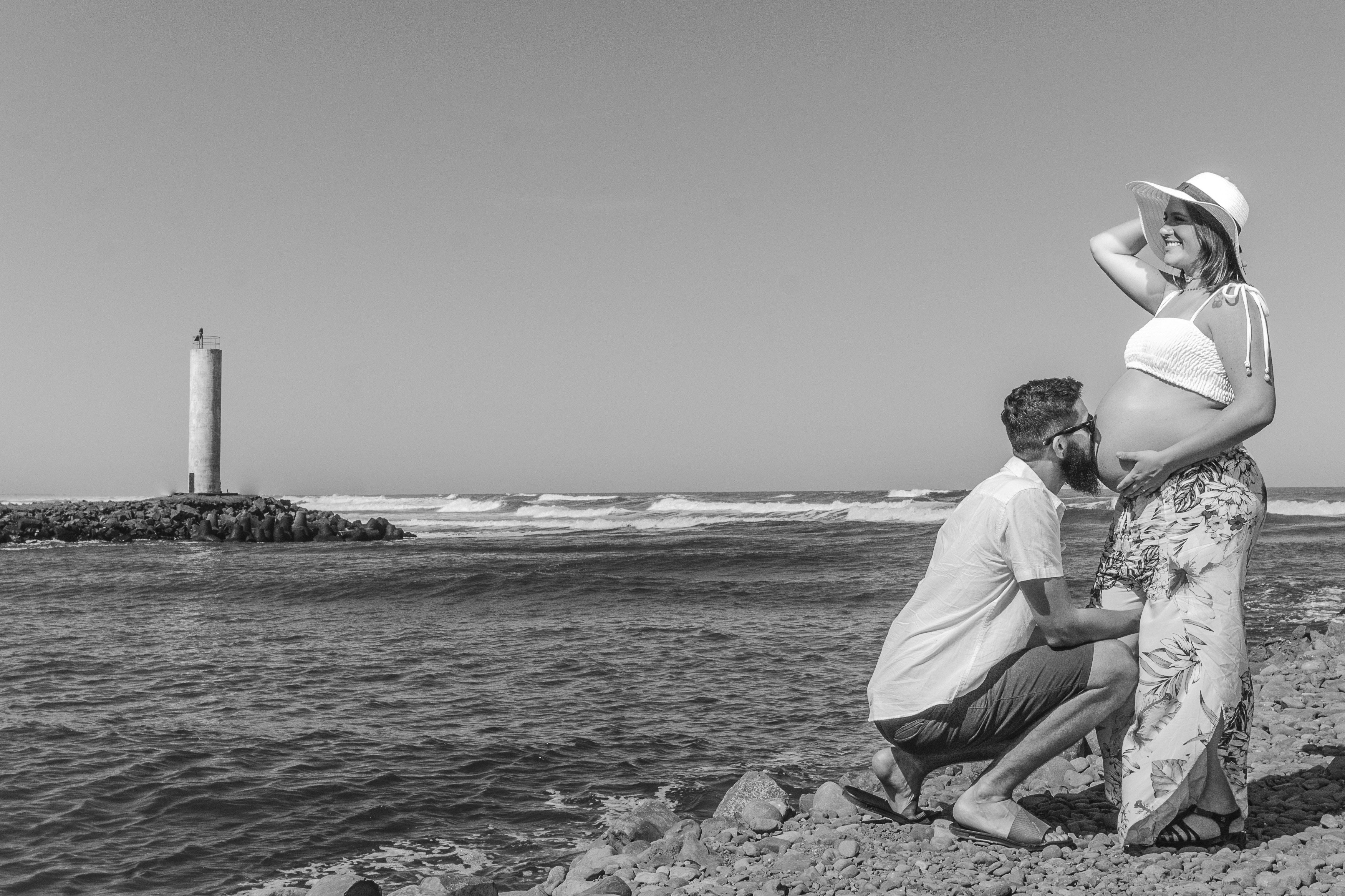 homem na camisa branca sentado na rocha perto do corpo de água durante o dia