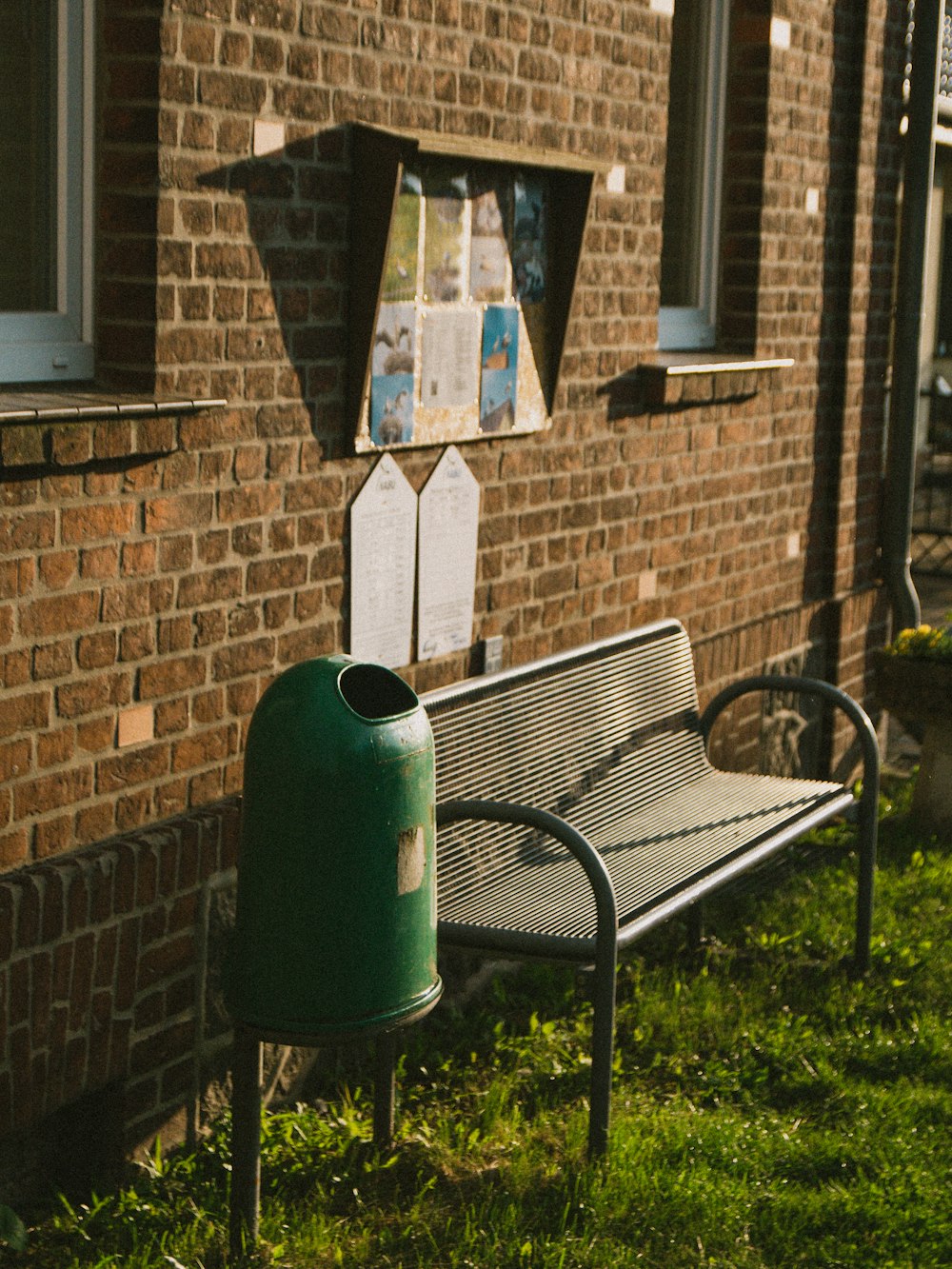 green metal trash bin beside brown brick wall