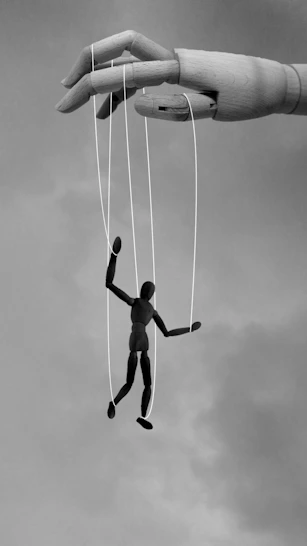 power-plays - A large wooden hand manipulating a small black mannequin with white strings