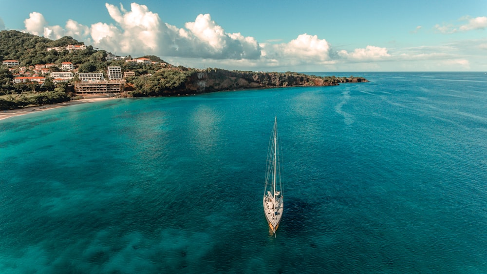 Barca a vela bianca e blu sul mare blu sotto il cielo nuvoloso blu e bianco durante il giorno