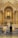 A couple in wedding attire is kneeling before an ornate and gilded church altar. The altar is adorned with white flowers, tall candles, and a central religious icon. The architecture features intricate details and gold accents, showcasing a blend of classical and religious elements.