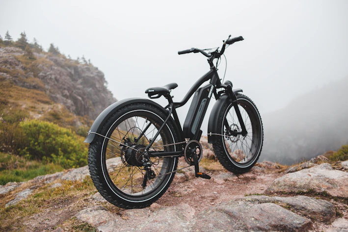 A sleek, vibrant electric mountain bike climbing a rugged trail bathed in morning light.