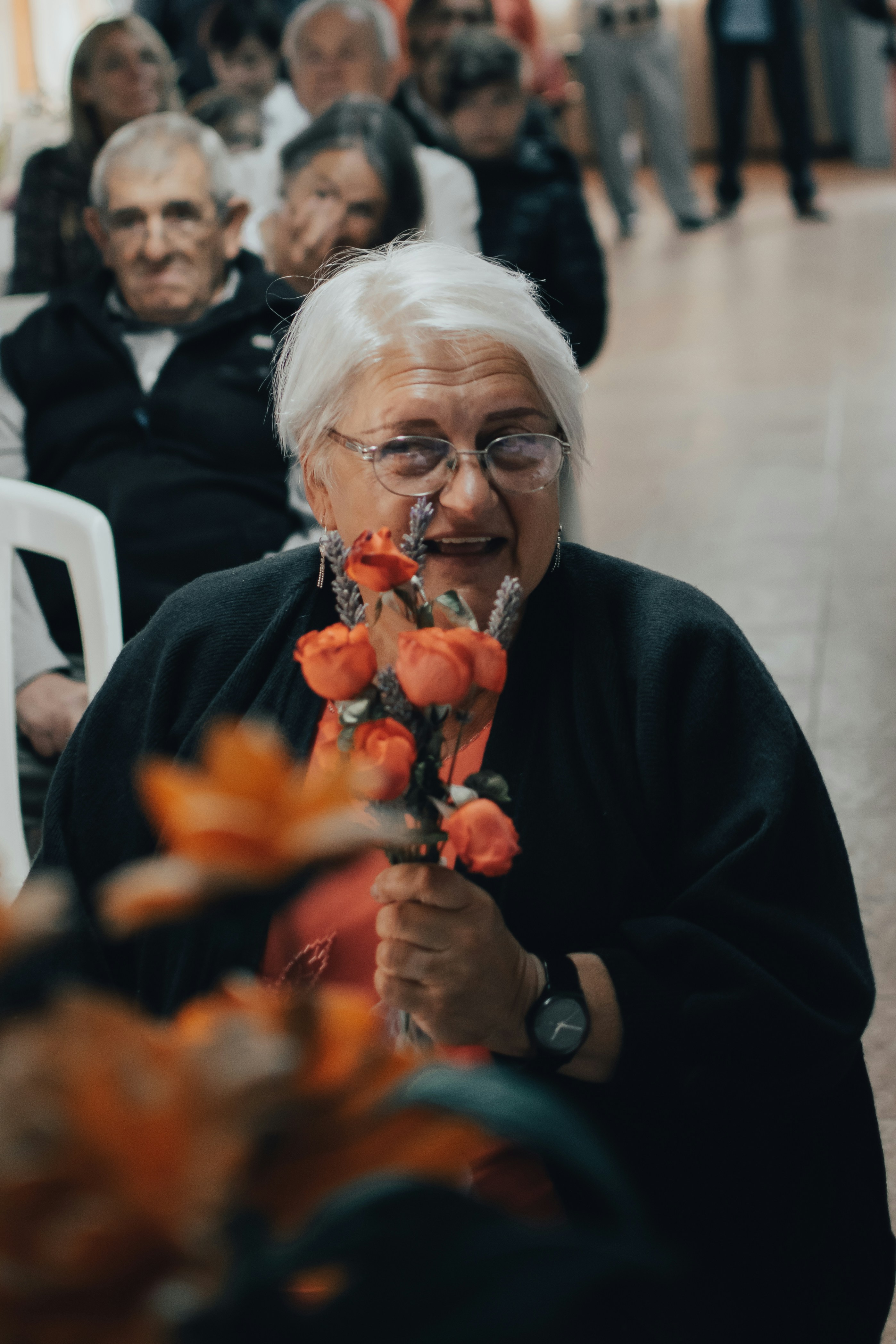 Elderly woman smiling while receiving flowers from a volunteer in a cozy home setting
