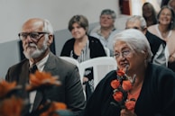 man in black suit jacket holding orange flower