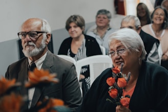 man in black suit jacket holding orange flower