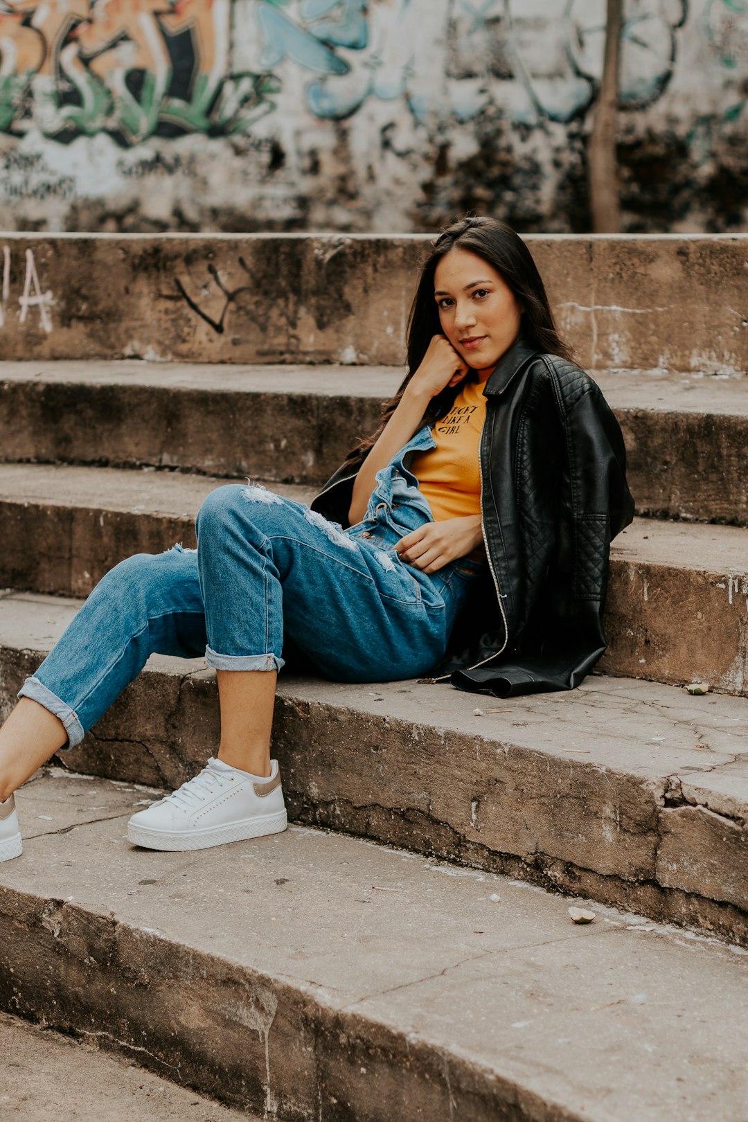 woman in black jacket and blue denim jeans sitting on concrete stairs
