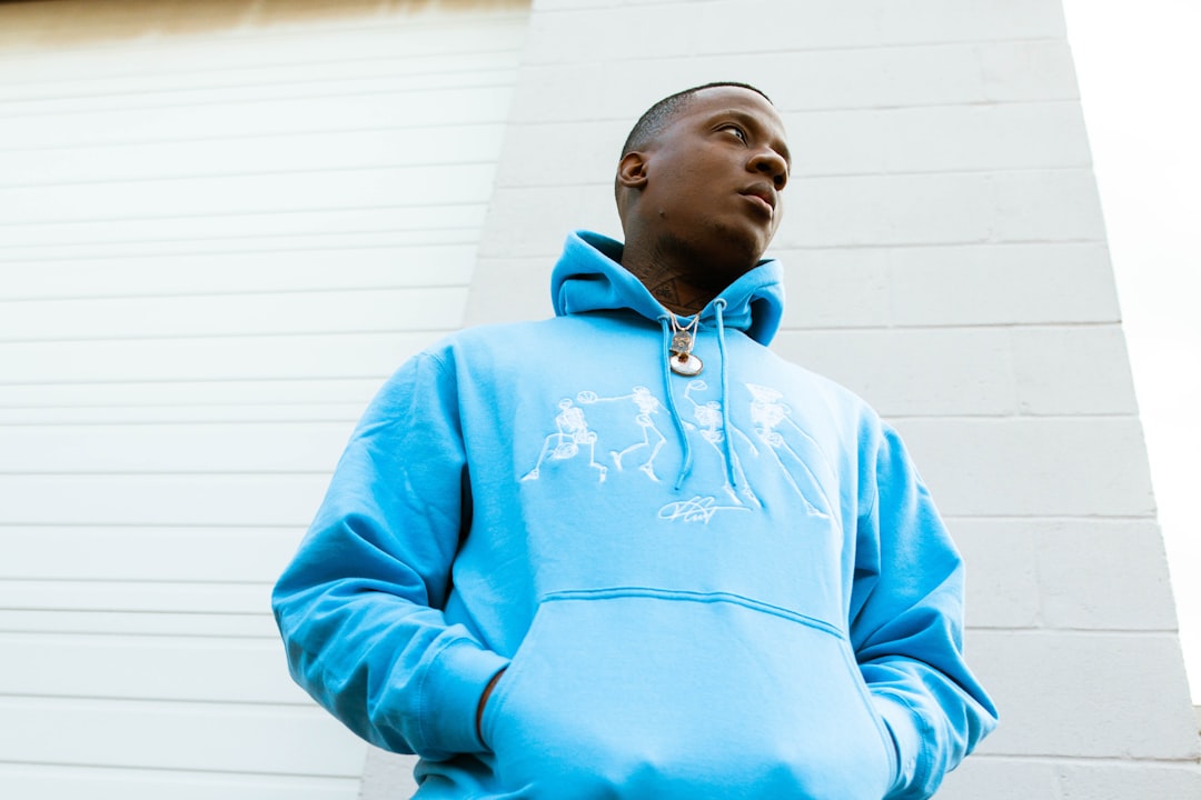 man in teal hoodie standing near white wall