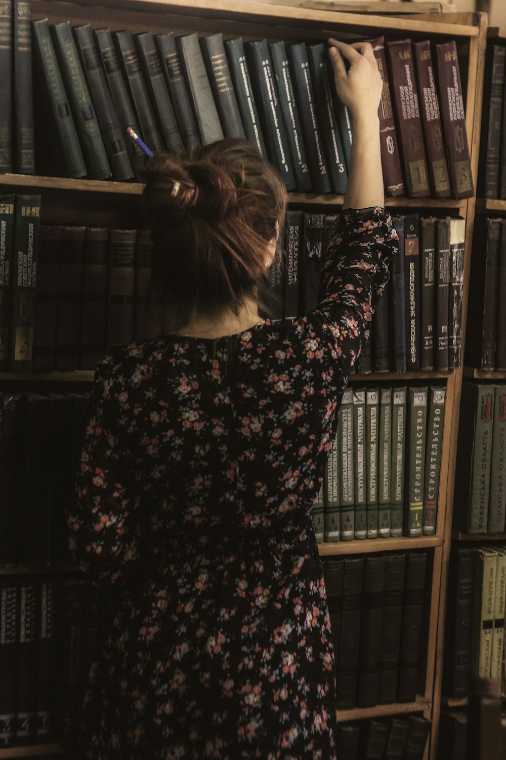 woman in black and red floral long sleeve dress standing near brown wooden book shelf