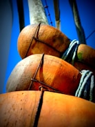 Several textured, orange and brown buoys are tightly bound together with black rope, set against a vibrant blue sky. A coiled green and blue rope is visible in the arrangement.