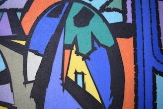 Abstract artwork featuring geometric shapes and bold lines in various colors including blue, green, orange, and purple. The composition has a textured appearance with overlapping forms creating a dynamic visual flow.