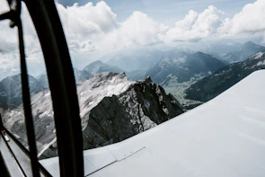 Close-up of a pilot smiling confidently mid-flight with rugged mountain peaks behind.
