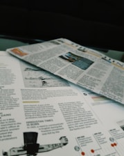 Newspapers and magazines are spread out, with text and images visible on the pages. One page has an article about historical topics, including a photo of an aircraft and a section discussing the inauguration of a political monument.