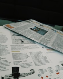 Newspapers and magazines are spread out, with text and images visible on the pages. One page has an article about historical topics, including a photo of an aircraft and a section discussing the inauguration of a political monument.