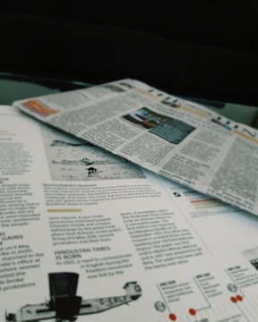 Newspapers and magazines are spread out, with text and images visible on the pages. One page has an article about historical topics, including a photo of an aircraft and a section discussing the inauguration of a political monument.