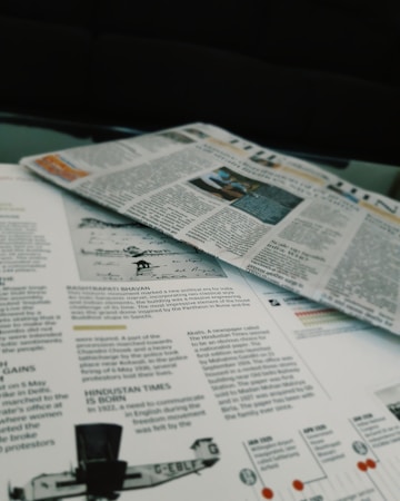 Newspapers and magazines are spread out, with text and images visible on the pages. One page has an article about historical topics, including a photo of an aircraft and a section discussing the inauguration of a political monument.