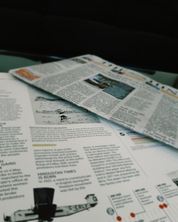 Newspapers and magazines are spread out, with text and images visible on the pages. One page has an article about historical topics, including a photo of an aircraft and a section discussing the inauguration of a political monument.