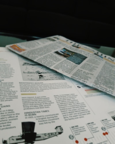 Newspapers and magazines are spread out, with text and images visible on the pages. One page has an article about historical topics, including a photo of an aircraft and a section discussing the inauguration of a political monument.