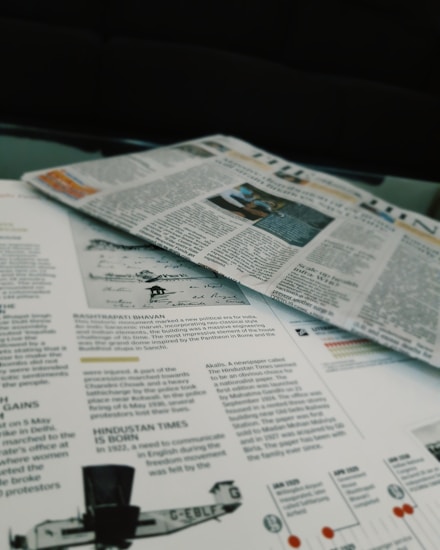 Newspapers and magazines are spread out, with text and images visible on the pages. One page has an article about historical topics, including a photo of an aircraft and a section discussing the inauguration of a political monument.