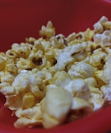 A close-up view of popped popcorn kernels filling a red bowl. The popcorn has a buttery and fluffy texture.