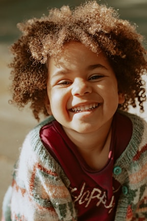 A smiling toddler wearing a cozy, hand-sewn sweater in a sunlit room.