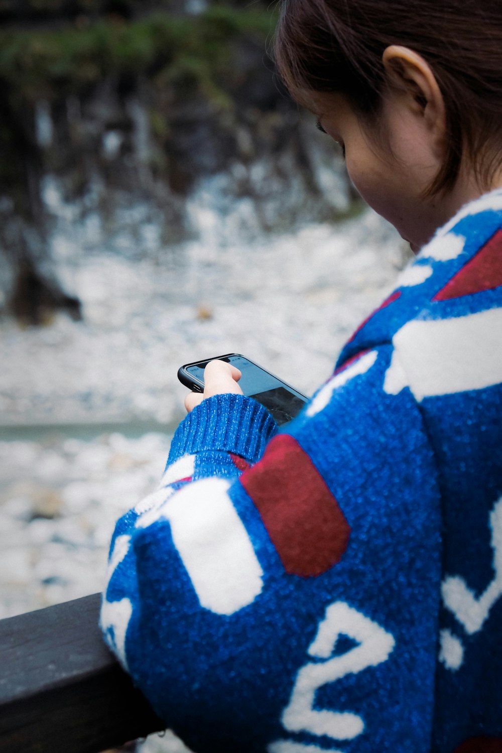 woman in blue and white sweater holding black smartphone