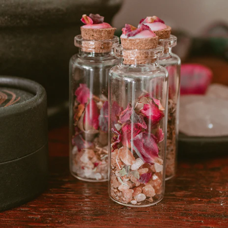 Delicate glass jars filled with earthy tinted pigments resting on a bed of dried flowers.