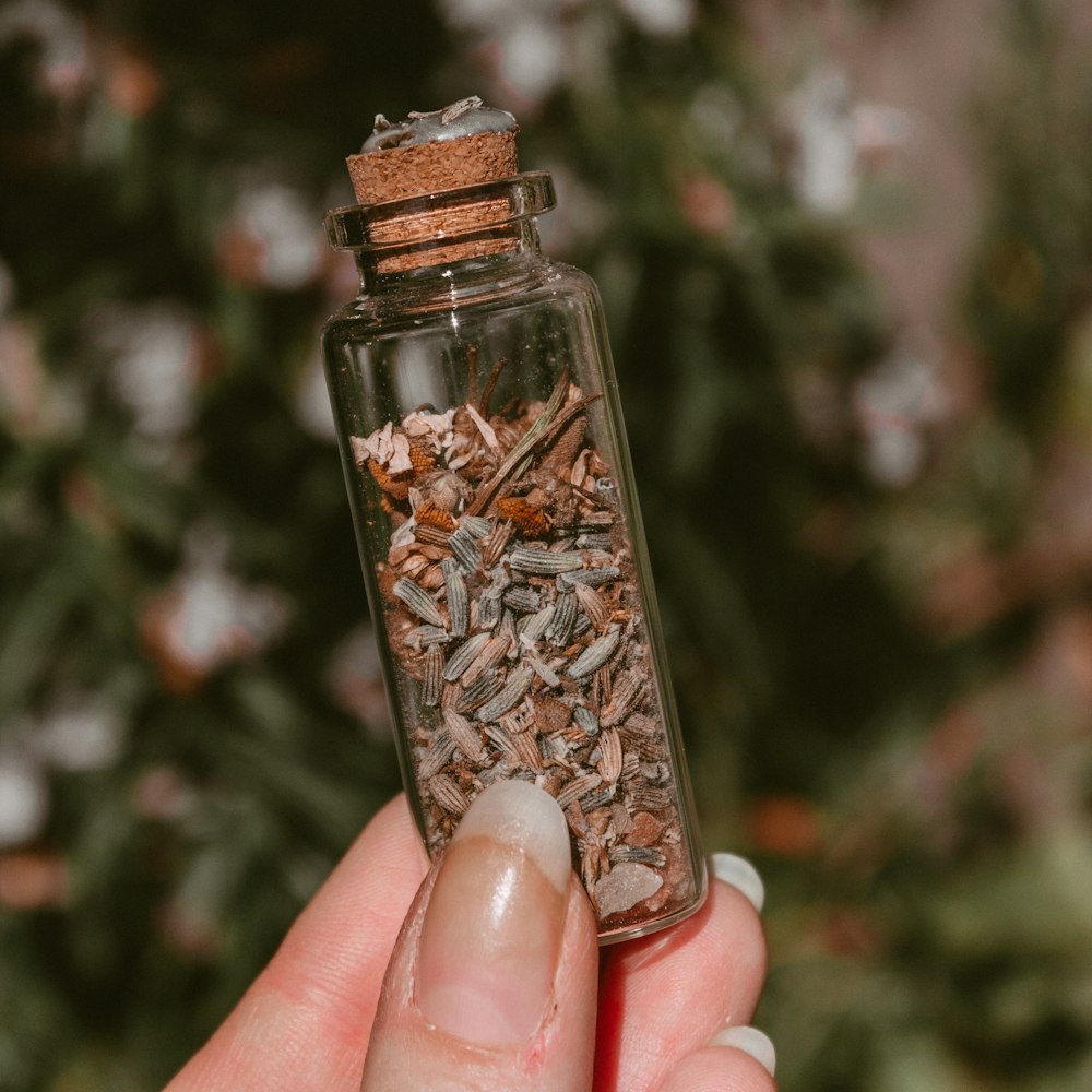 person holding clear glass bottle with brown powder