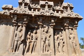 Intricate stone carvings depict a series of human figures in traditional attire, framed by ornate columns. The structure showcases detailed craftsmanship with multiple layers of sculpted figures, highlighting a historical or cultural narrative.