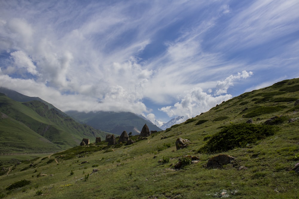 green grass field and mountains under white clouds and blue sky during daytime