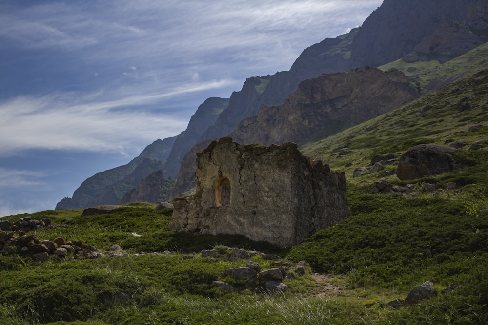 brown concrete building on green grass field near mountain under white clouds and blue sky during