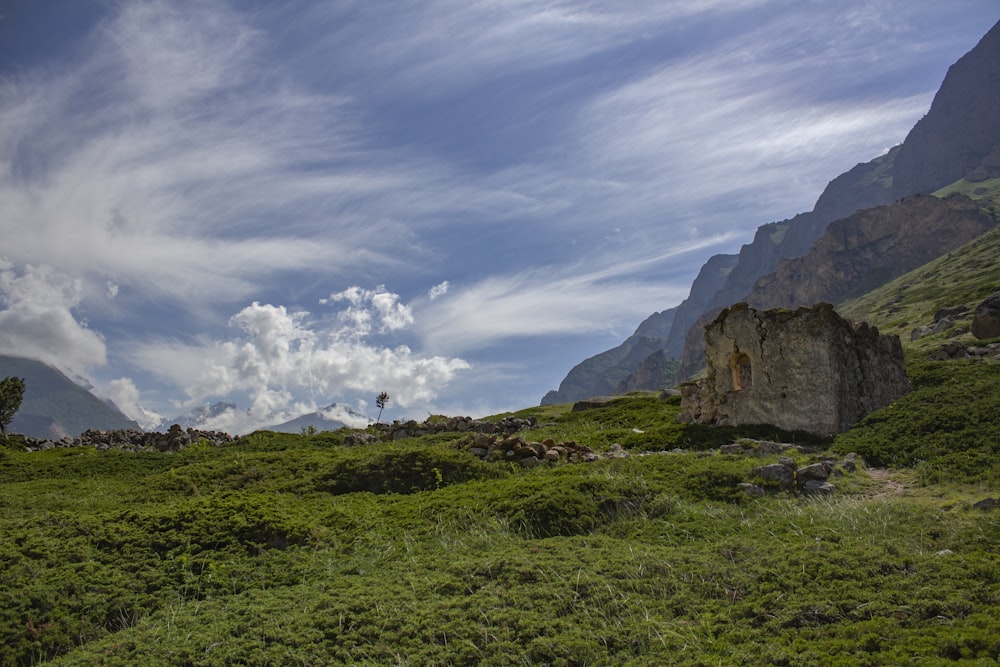 green grass field near brown rock formation under white clouds and blue sky during daytime