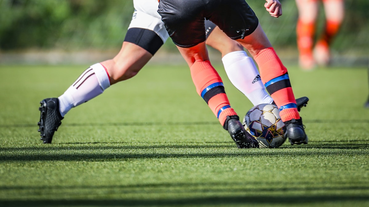 woman in black and white soccer jersey kicking soccer ball on green field during daytime