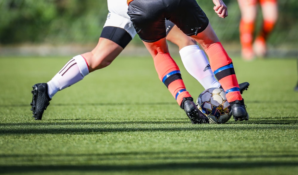 Donna in maglia da calcio in bianco e nero che calcia il pallone da calcio sul campo verde durante il giorno