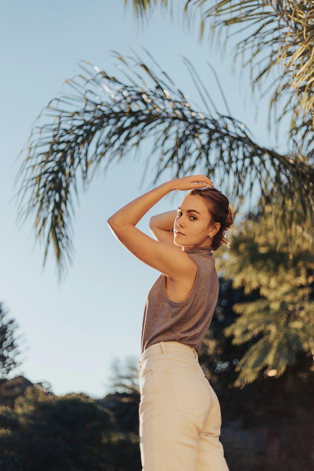 woman in gray tank top and white shorts standing near palm tree during daytime