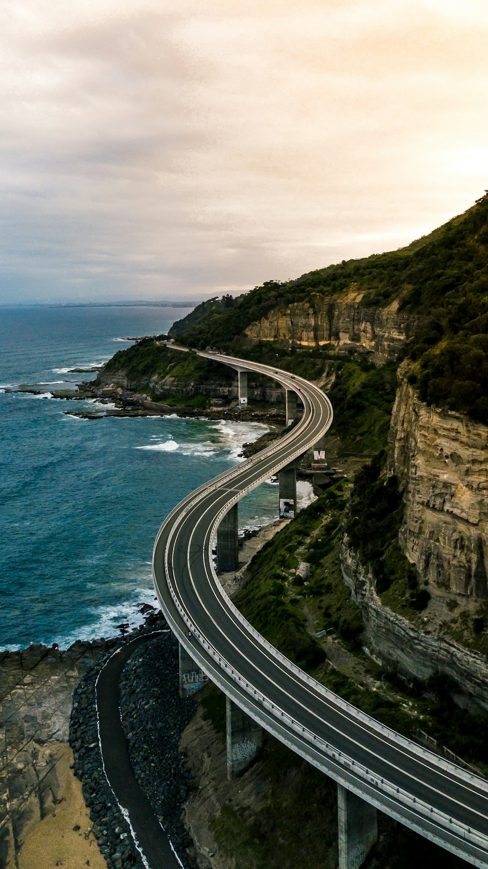 gray concrete road near cliff and body of water during daytime