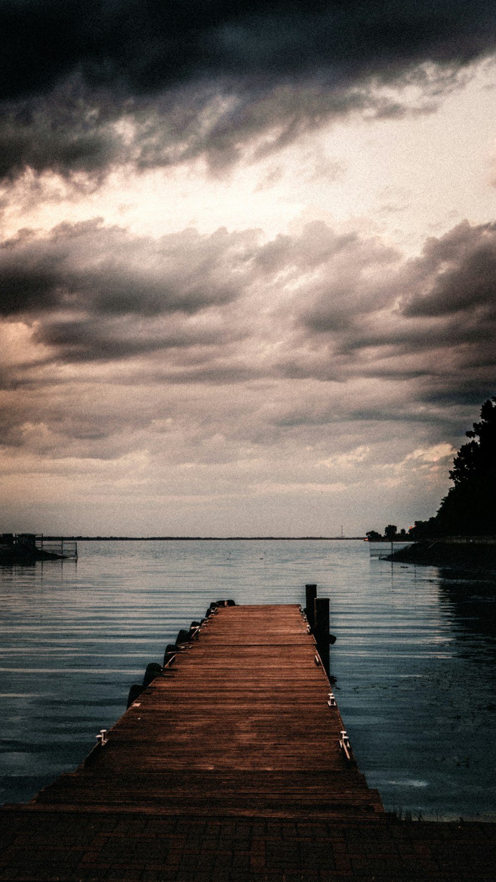 brown wooden dock on body of water under cloudy sky during daytime