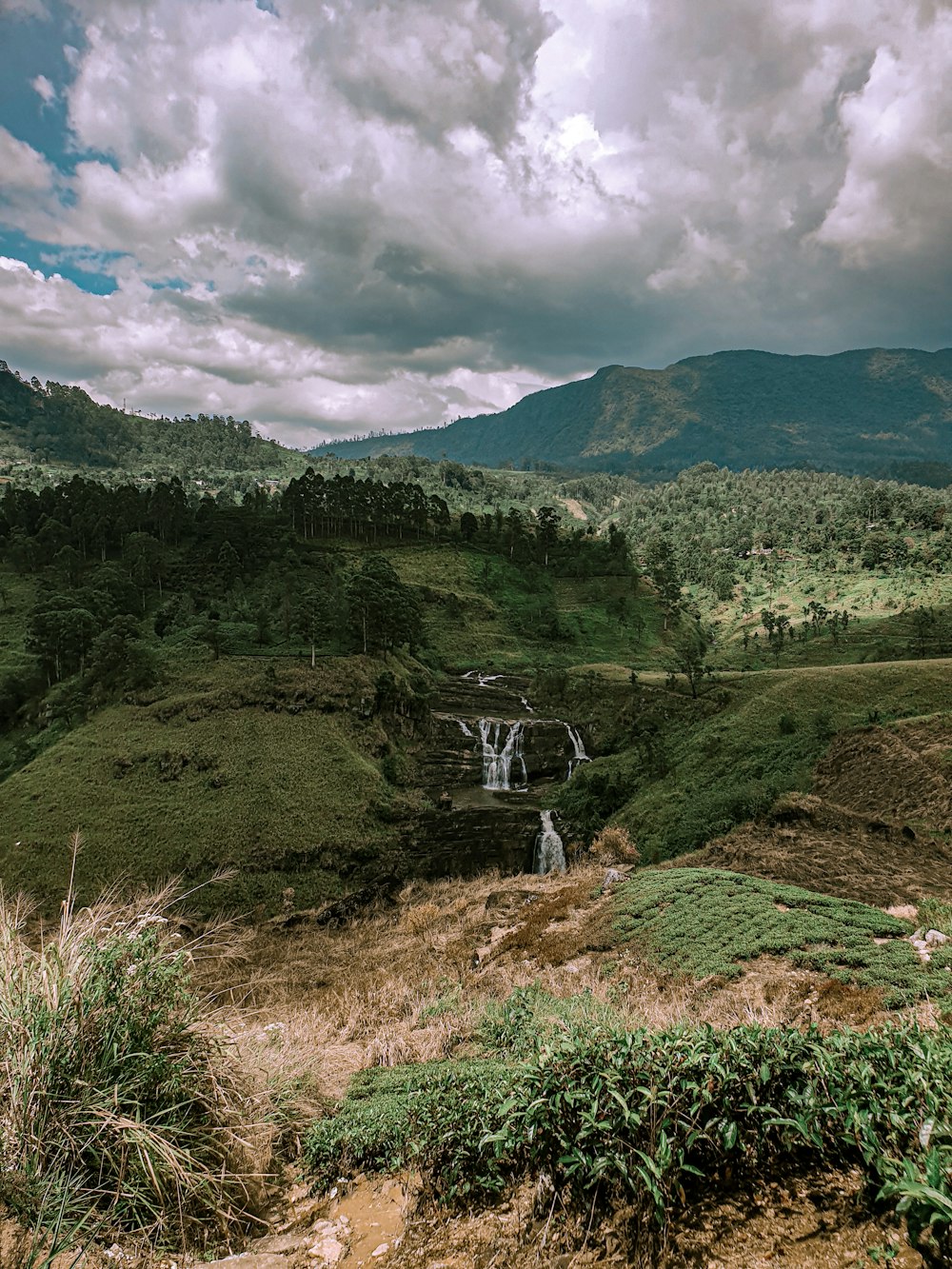 green grass field and mountain under white clouds and blue sky during daytime