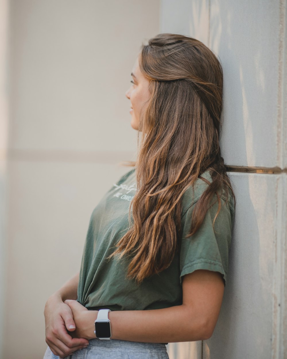 woman in green shirt leaning on white wall