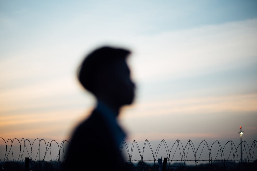silhouette of man standing near fence during sunset