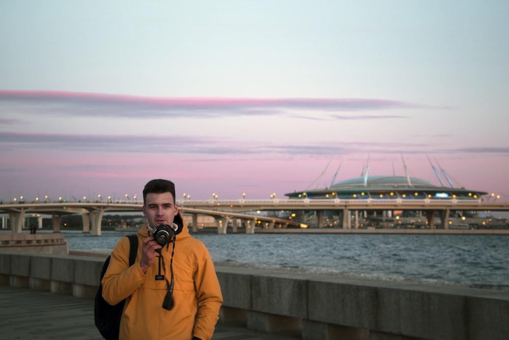 man in orange jacket holding black dslr camera