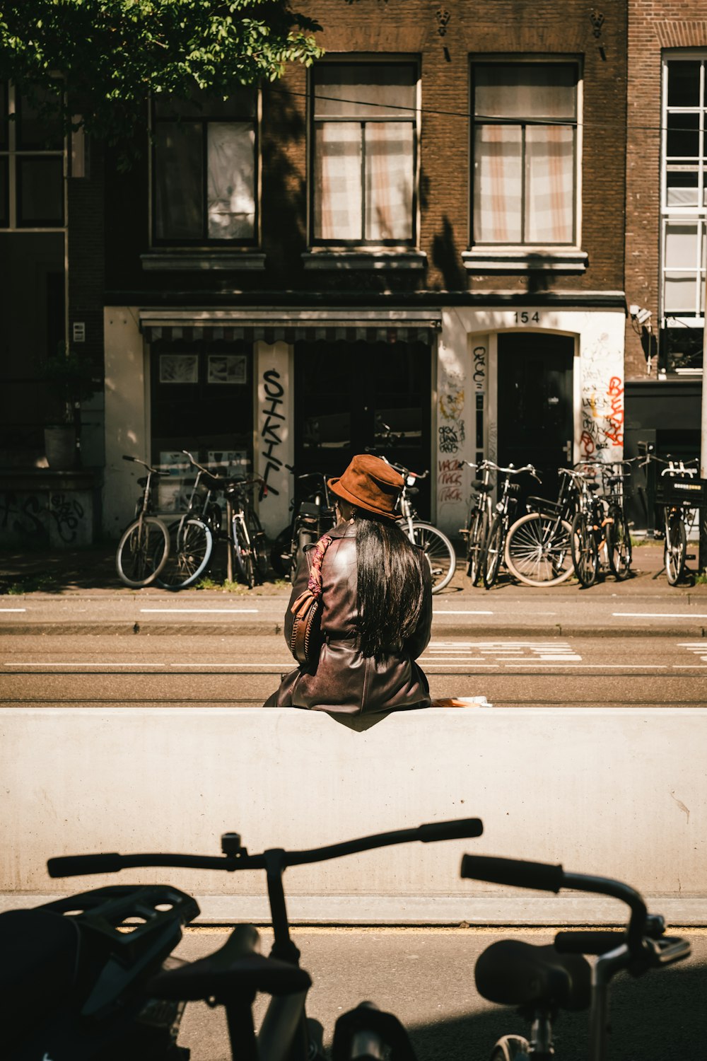 woman in black hat and black jacket sitting on sidewalk during daytime