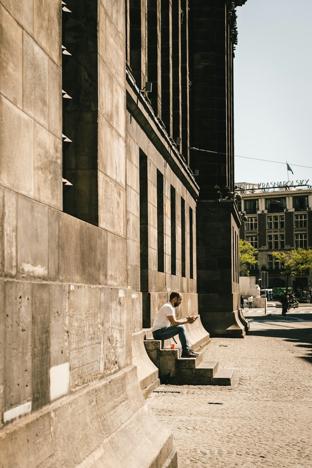 Homme en veste noire assis sur un banc près d’un bâtiment pendant la journée