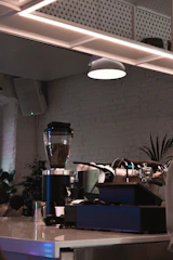 A sleek, modern café interior with dark tones, soft lighting, and a barista preparing coffee beside a digital AI interface.