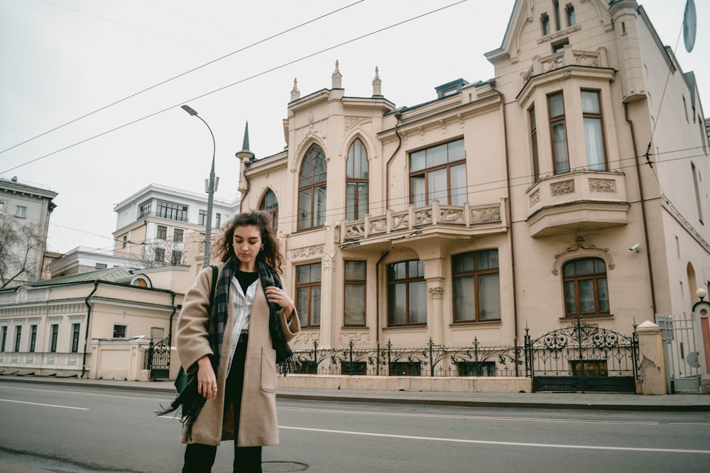 woman in brown coat standing on sidewalk during daytime