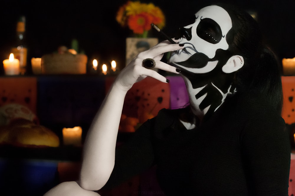 person in black and white skull mask holding lighted candle
