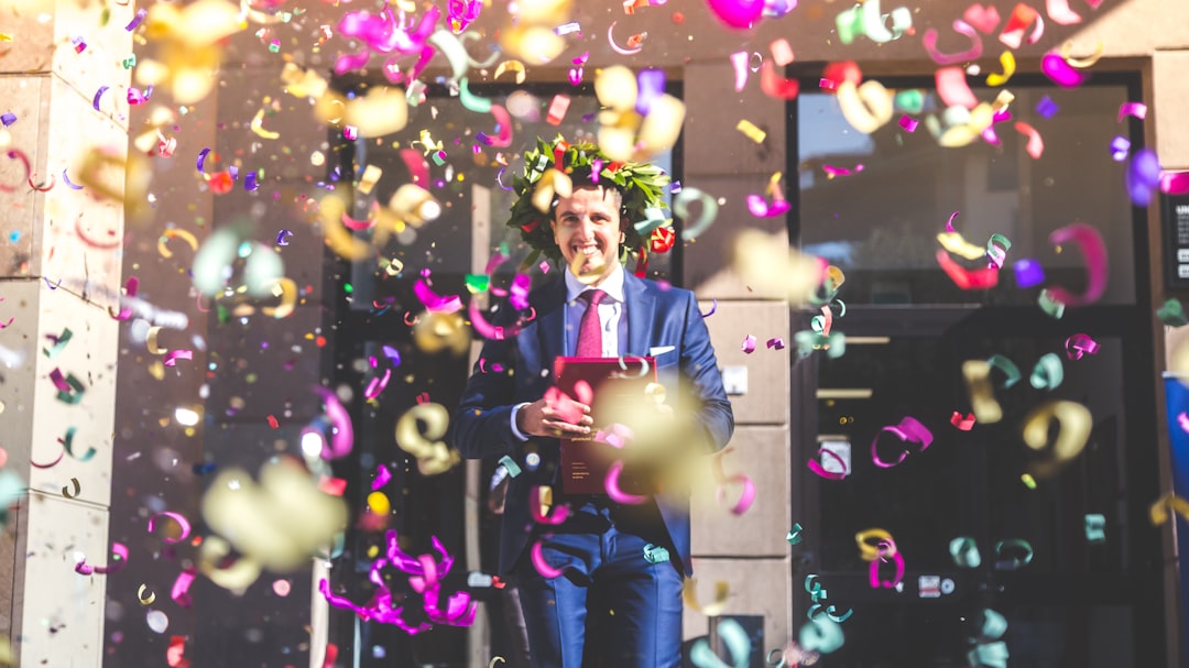 man in black suit jacket and blue denim jeans holding green and pink balloons
