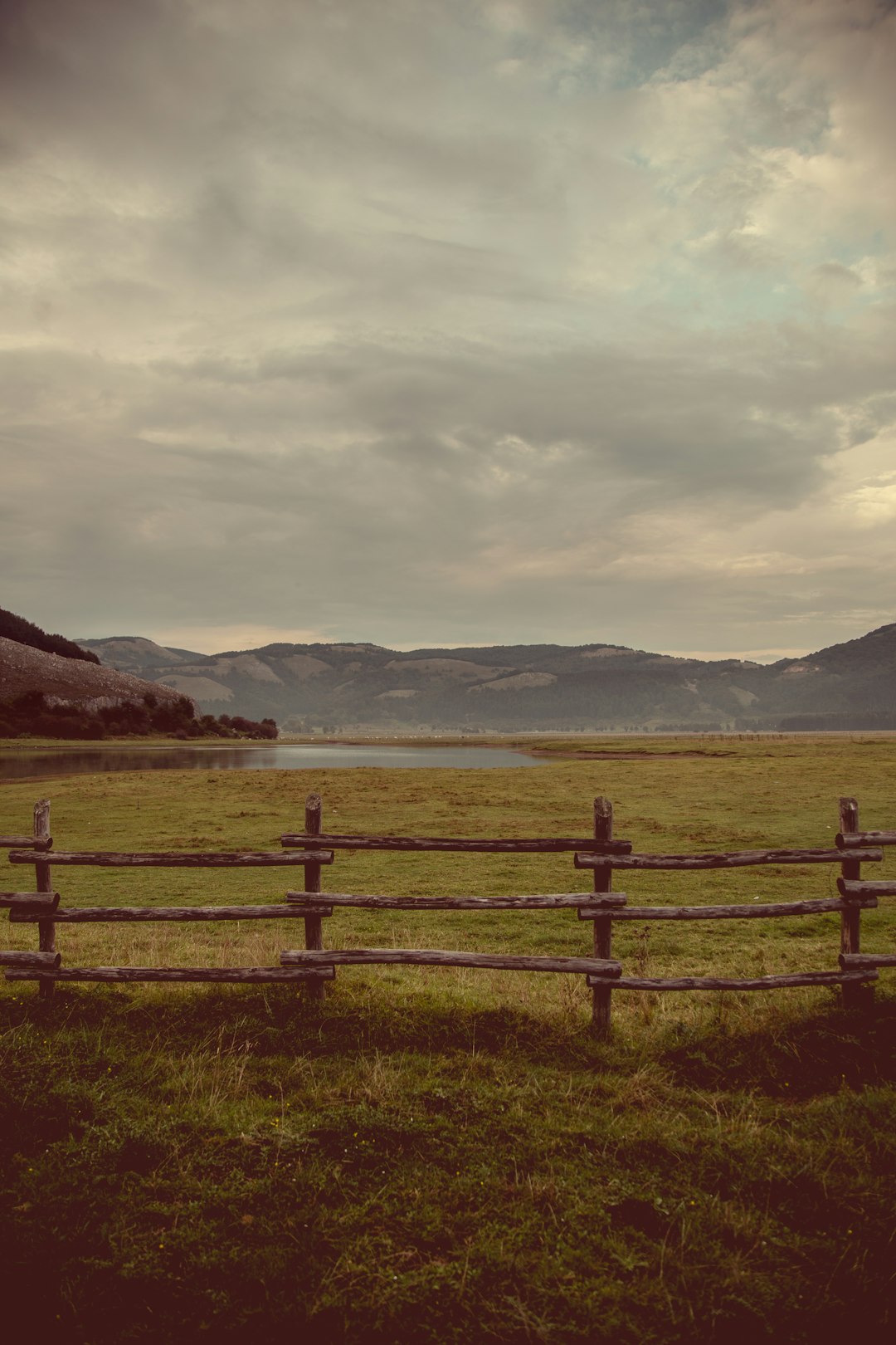 brown wooden fence on green grass field near body of water under white clouds during daytime