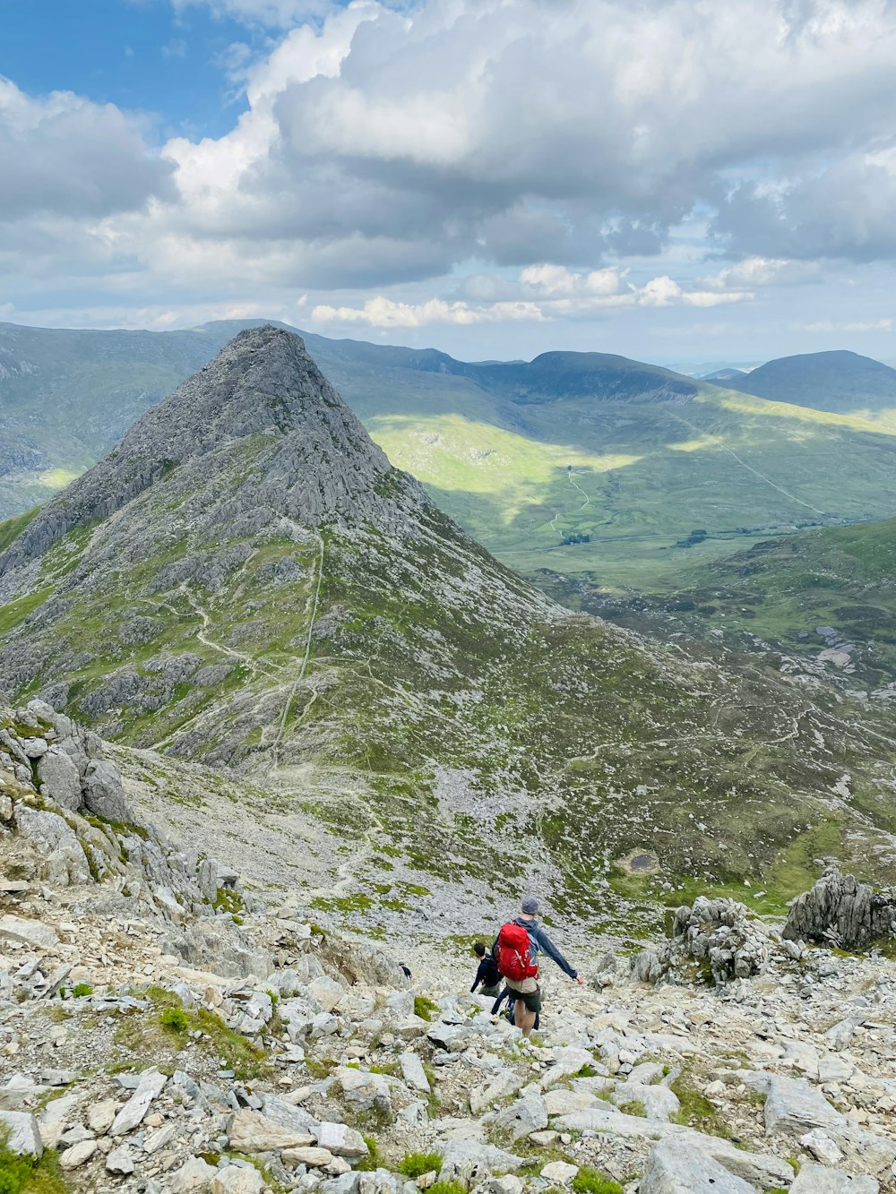 person in red jacket and black pants standing on rocky mountain during daytime